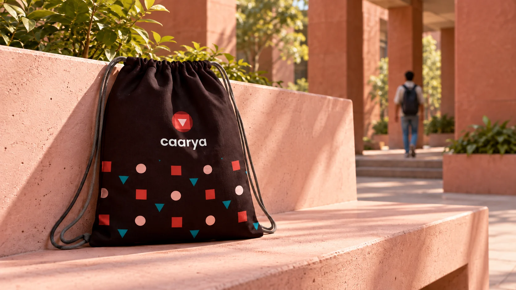 Caarya drawstring bag mockup on a sunlit campus bench, with its red, pink and teal geometric pattern.